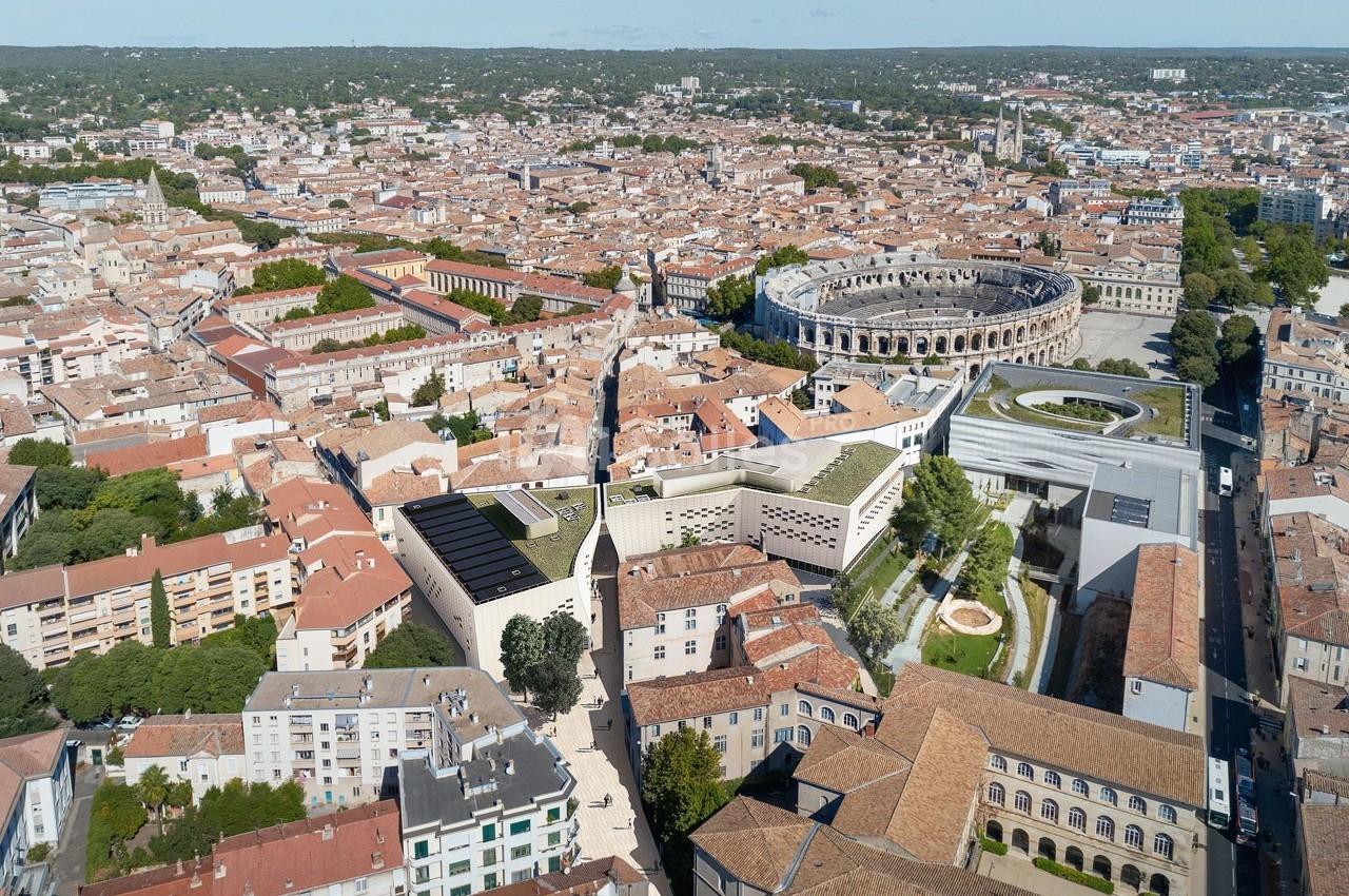 Vue aérienne de la ville de Nîmes, montrant les toits, les arènes romaines et des bâtiments modernes environnants.