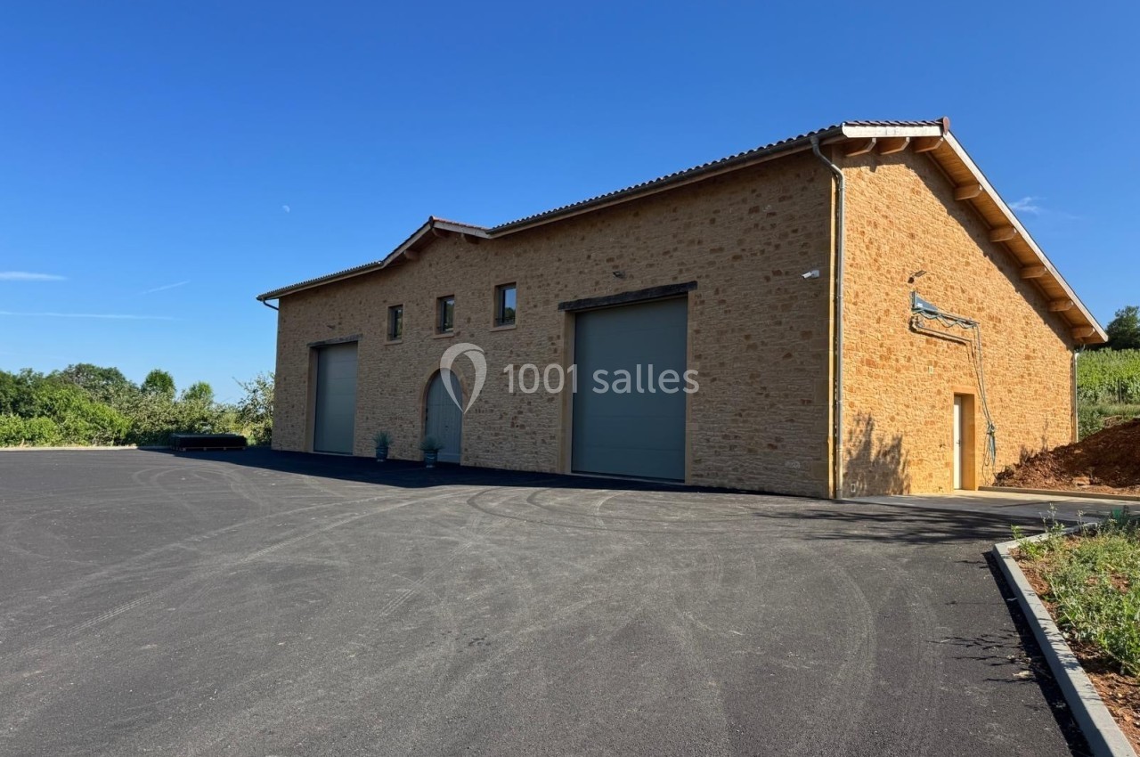 Bâtiment en pierre avec trois grandes portes, situé sur une large surface asphaltée sous un ciel dégagé.