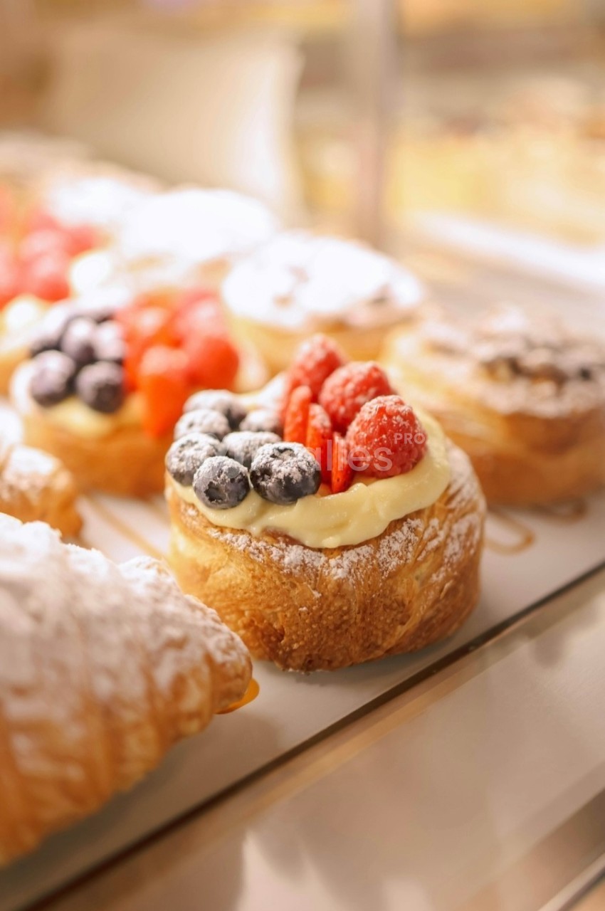 Pâtisseries garnies de crème, framboises et myrtilles, disposées sur un présentoir en vitrine.