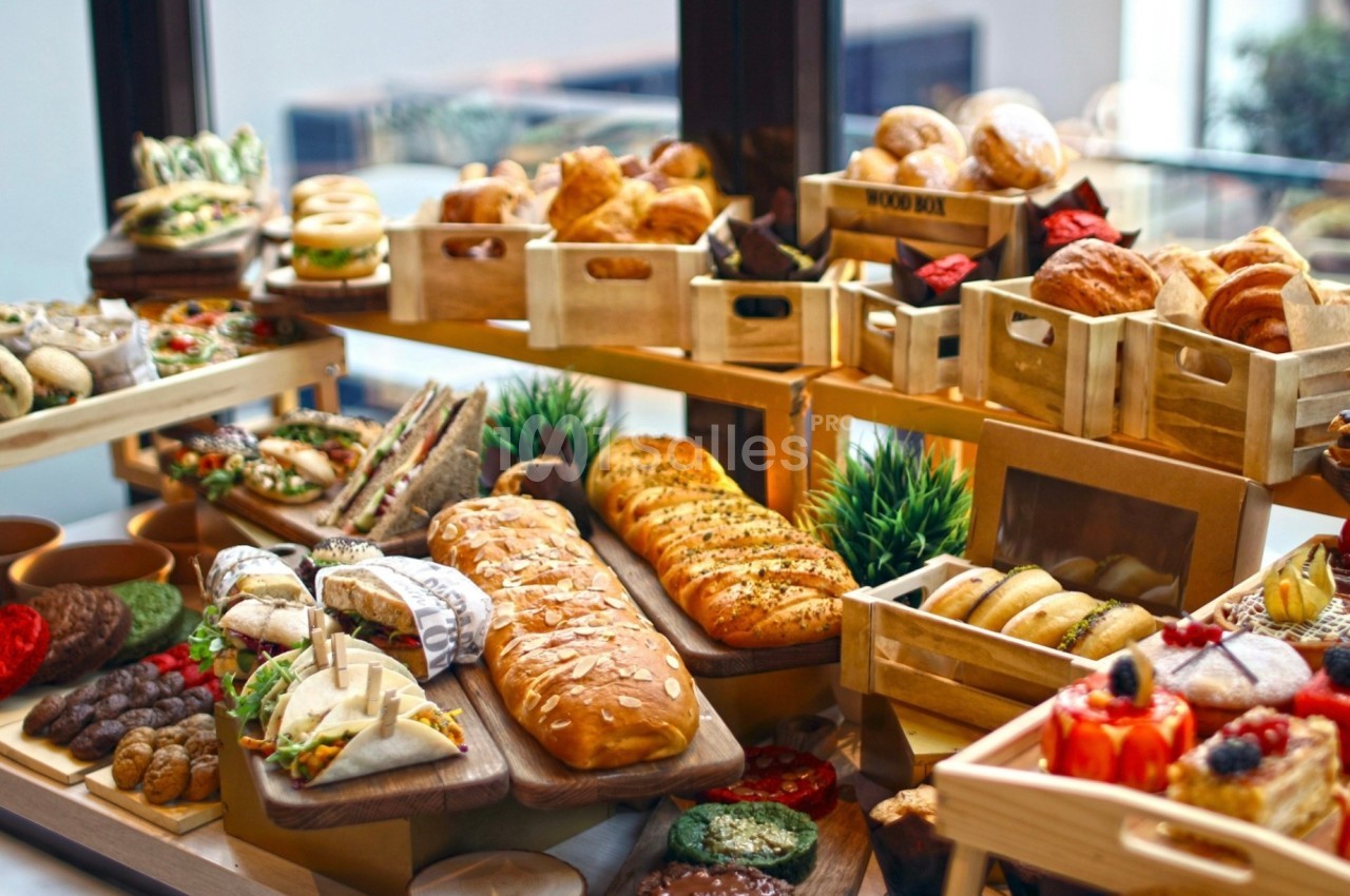 Table garnie de pains, viennoiseries, sandwichs et fruits présentés dans des caisses en bois et sur des plateaux.