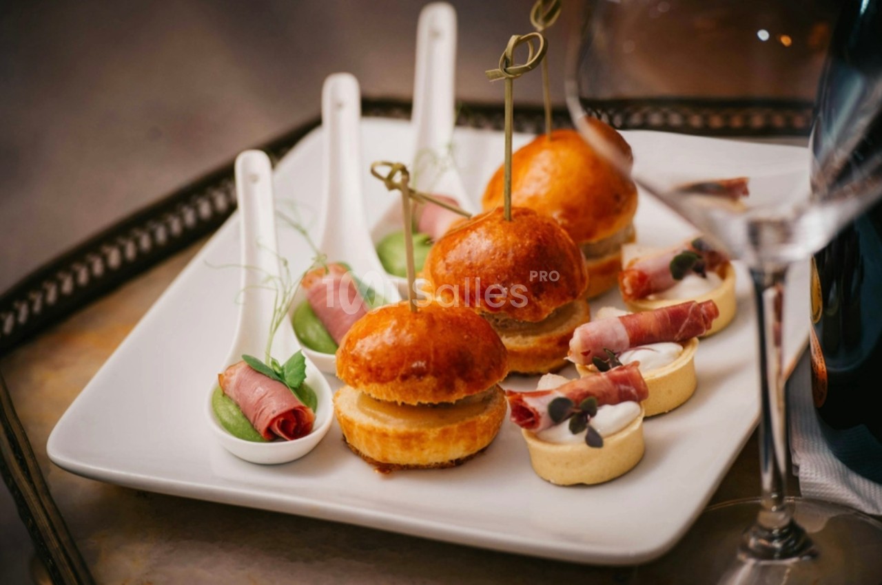 Assortiment d'amuse-bouches comprenant mini-burgers, cuillères garnies et tartelettes sur une assiette blanche.