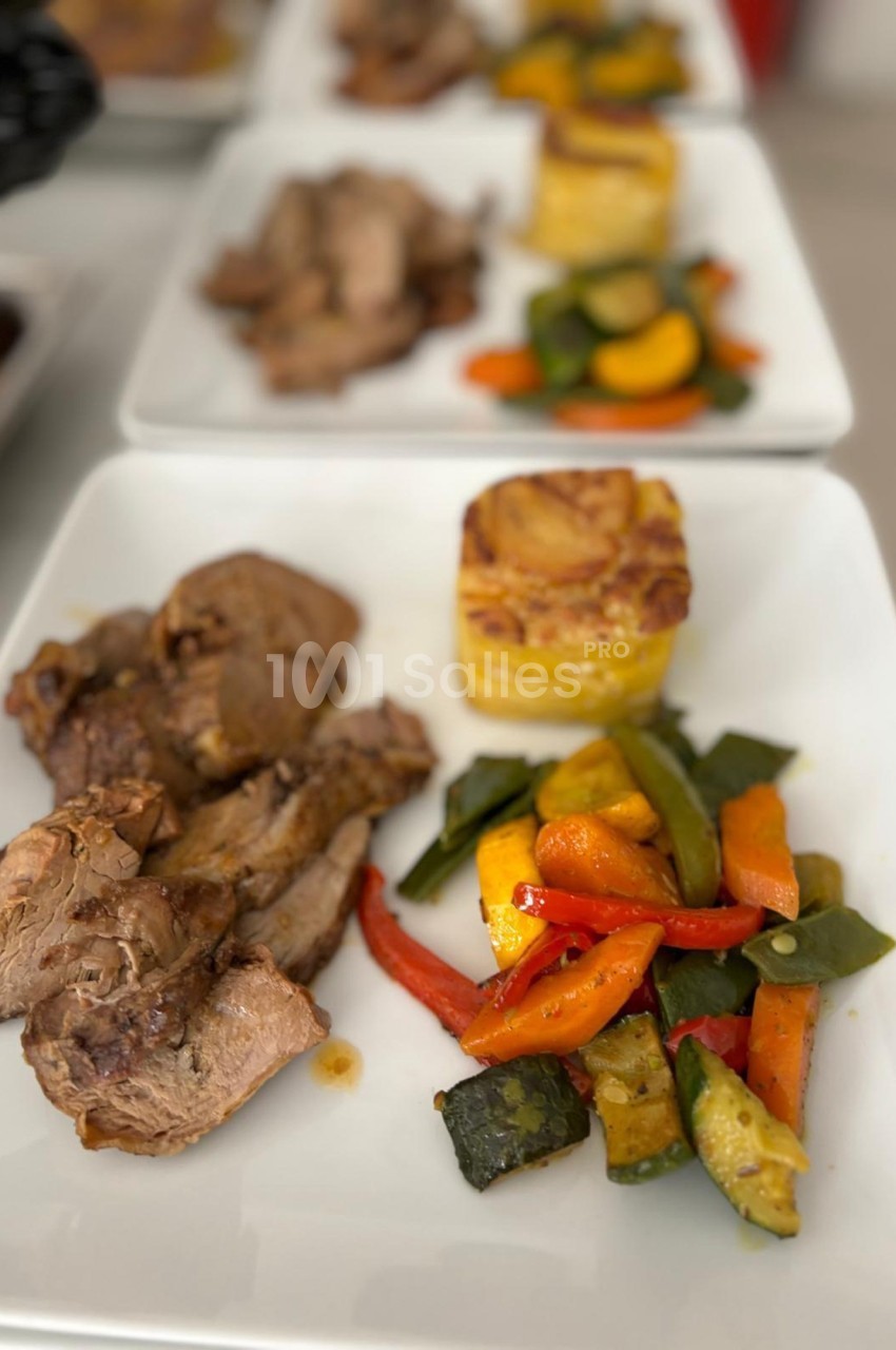 Assiette composée de viande rôtie, légumes grillés colorés et gratin de pommes de terre, servie sur une table.