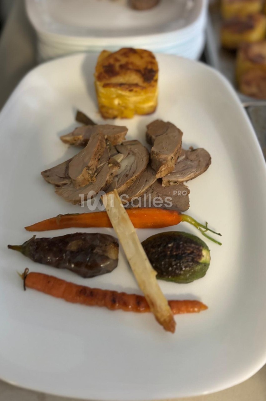 Assiette composée de tranches de viande, légumes rôtis variés et gratin de pommes de terre, présentée sur un plat blanc.