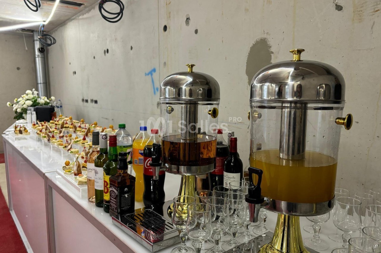 Buffet avec boissons variées, jus, sodas et snacks disposés sur une table dans un espace en cours de rénovation.