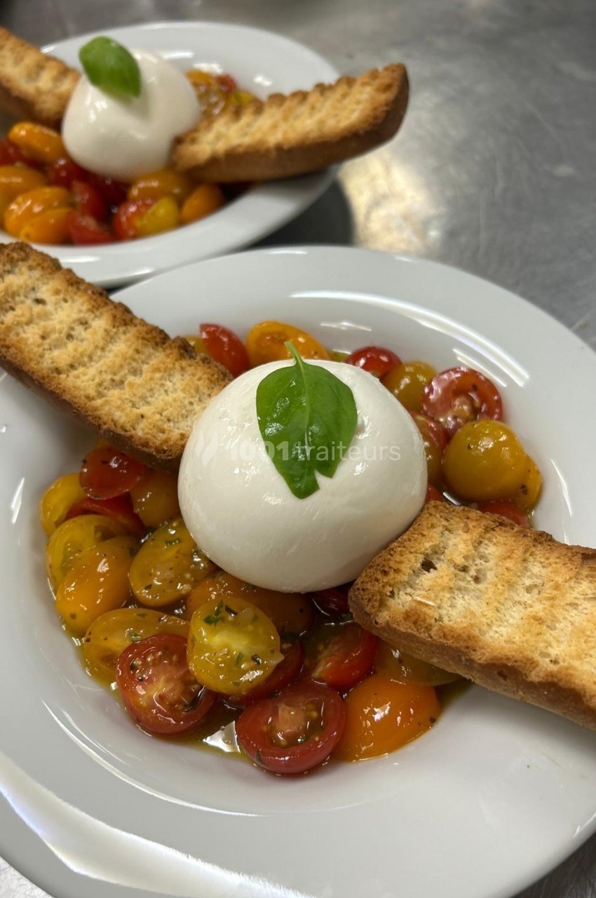 Assiette de tomates cerises colorées, burrata garnie de basilic et tranches de pain grillé.