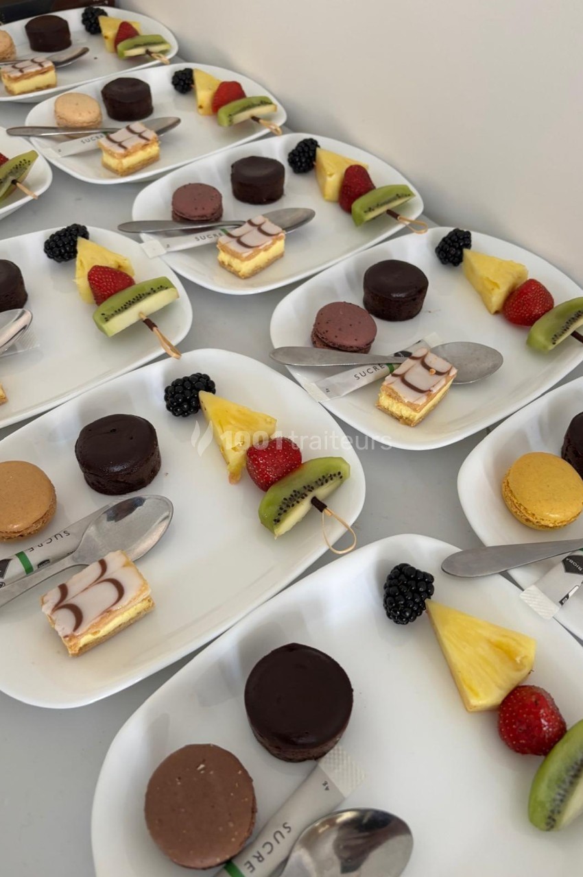 Assortiment de desserts individuels avec macarons, fruits frais et pâtisseries sur des assiettes blanches alignées.