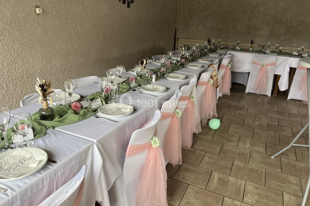 Tables décorées pour un événement, avec nappes blanches, chemins de table verts, chaises ornées de tissu rose et vaisselle…