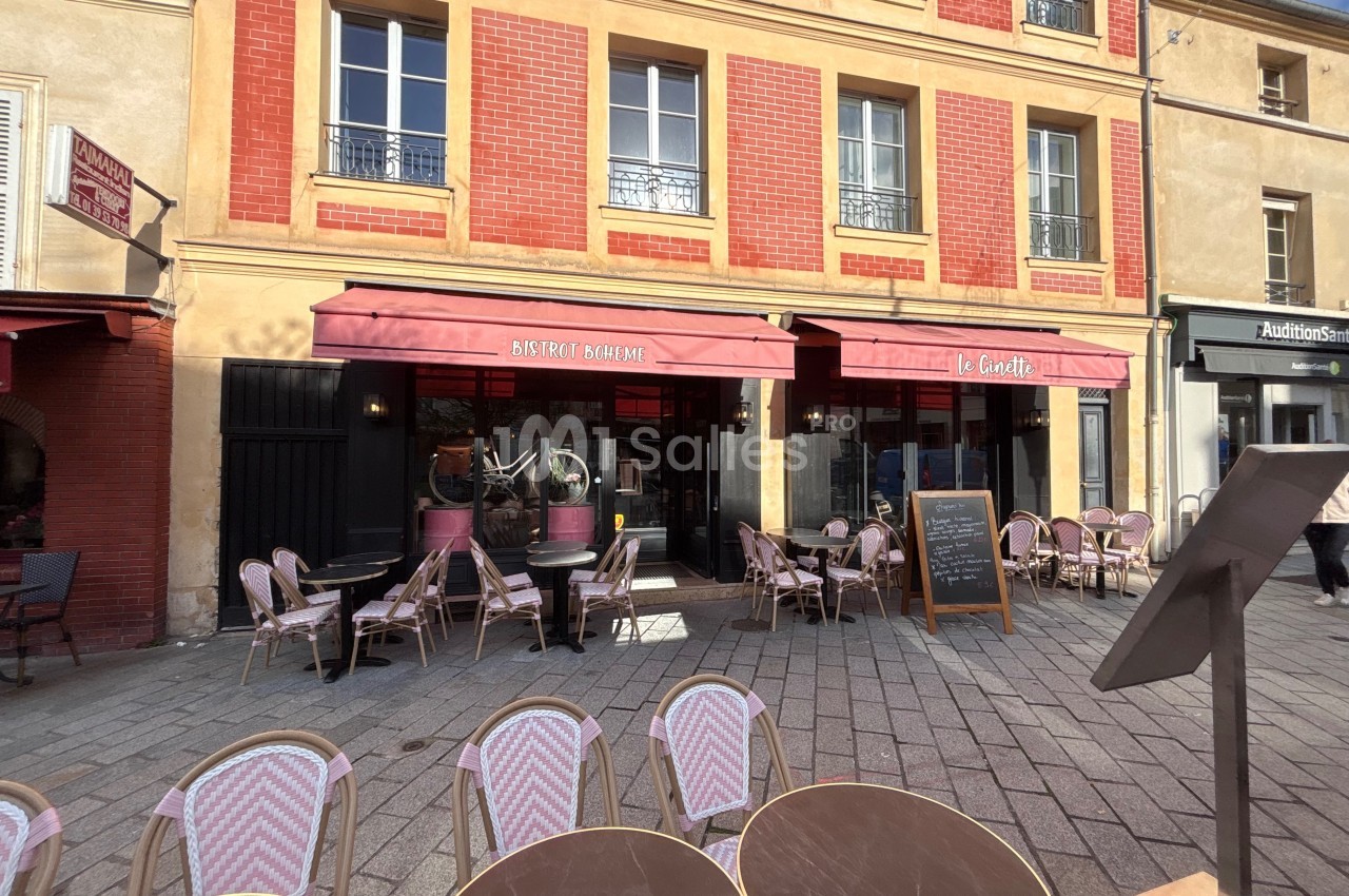 Façade d'un bistrot avec terrasse extérieure, tables et chaises en osier, situé dans une rue pavée.