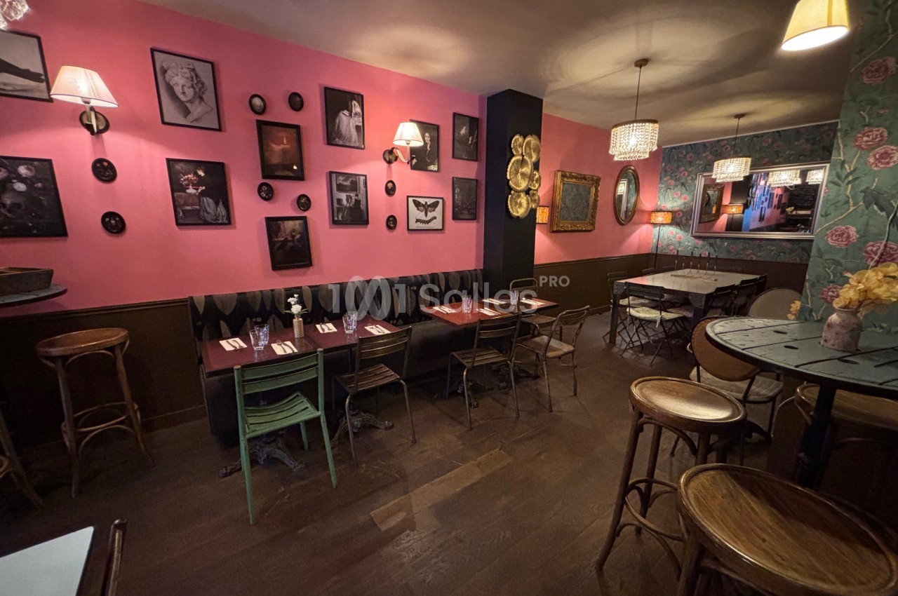Salle de restaurant chaleureuse avec murs décorés de cadres, tables en bois et éclairage tamisé.