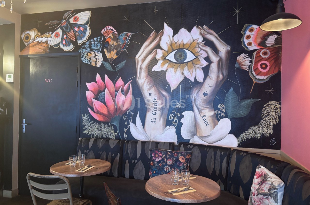 Fresque murale représentant des mains tenant une fleur avec un œil, entourée de papillons et de motifs floraux.