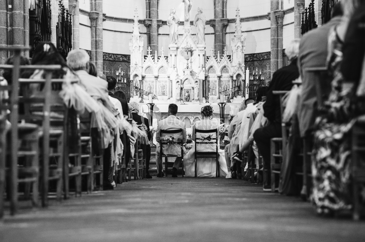 Vue arrière d'un couple assis devant l'autel lors d'une cérémonie religieuse dans une église.