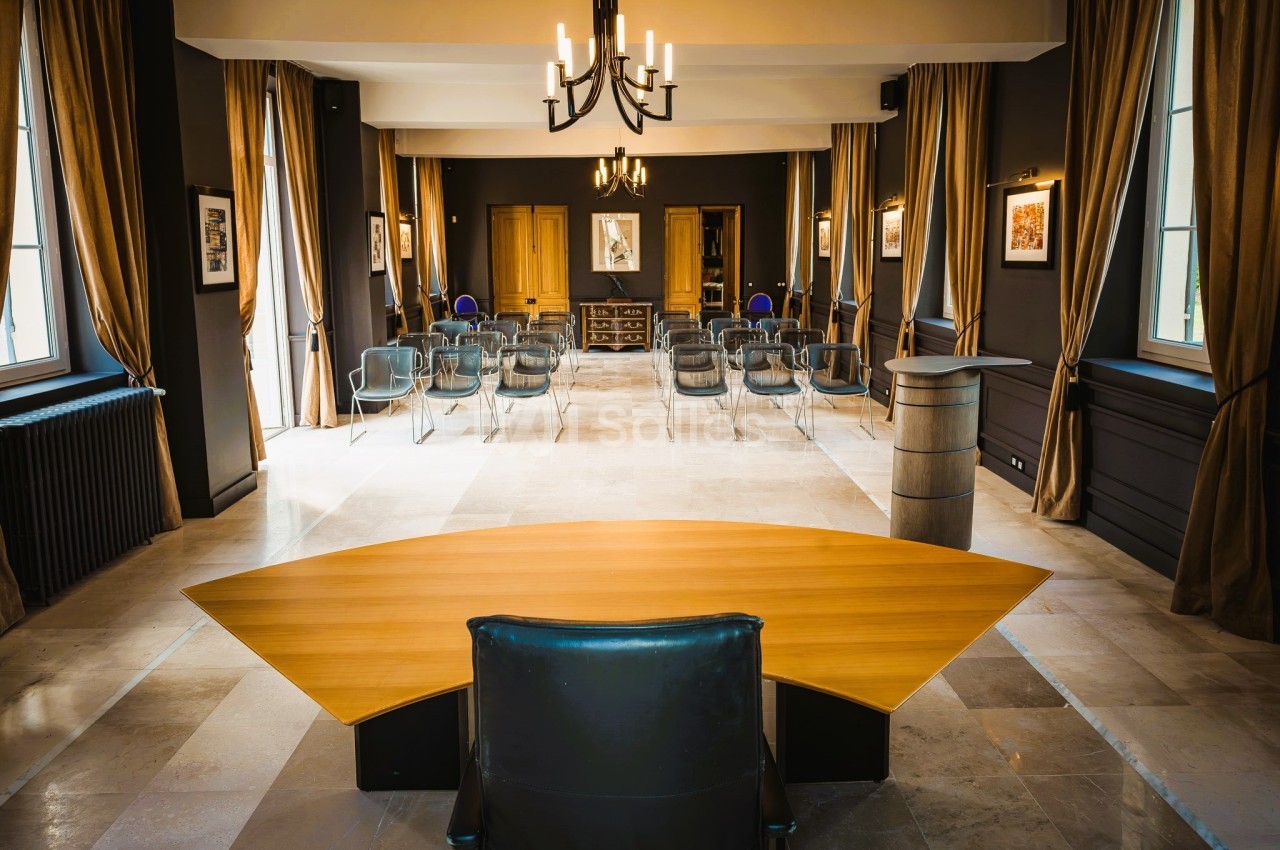 Salle de conférence lumineuse avec chaises alignées, rideaux dorés et bureau en bois au premier plan.