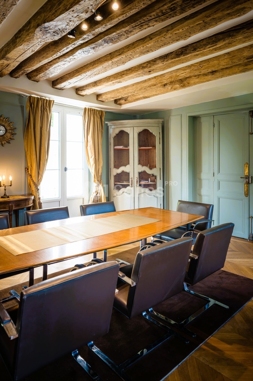 Salle à manger avec table en bois, chaises modernes, poutres apparentes au plafond et lumière naturelle.