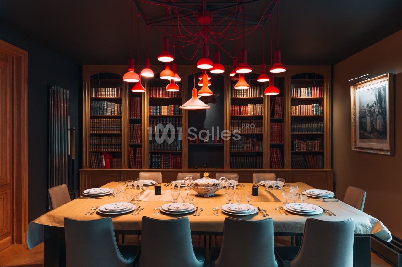 Salle à manger élégante avec une grande table dressée, entourée de chaises et éclairée par des suspensions rouges.