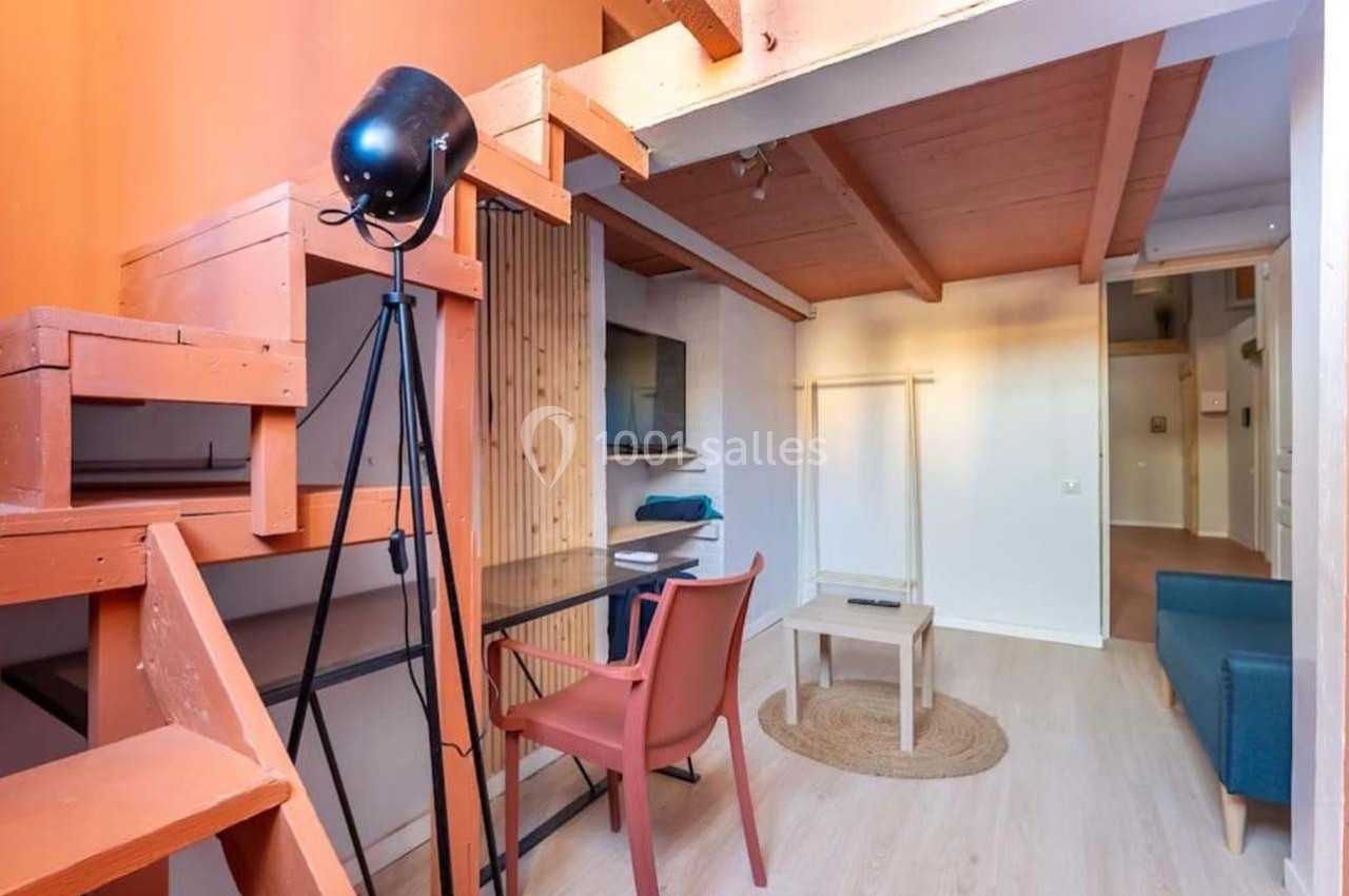 Espace de vie avec bureau, chaise, canapé, télévision murale et mezzanine en bois dans un intérieur lumineux.