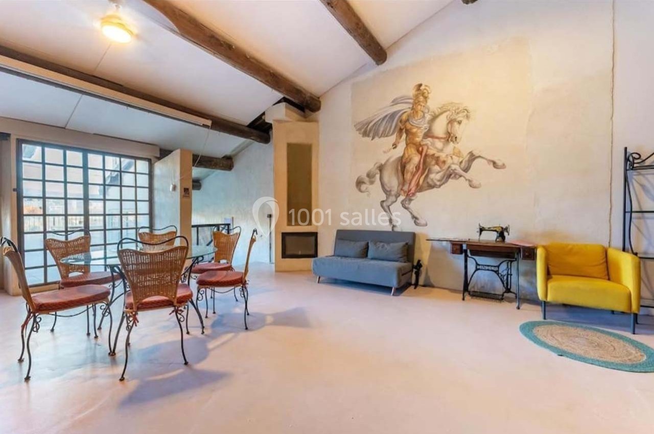 Salle lumineuse avec poutres apparentes, fresque murale, mobilier éclectique et grande baie vitrée.