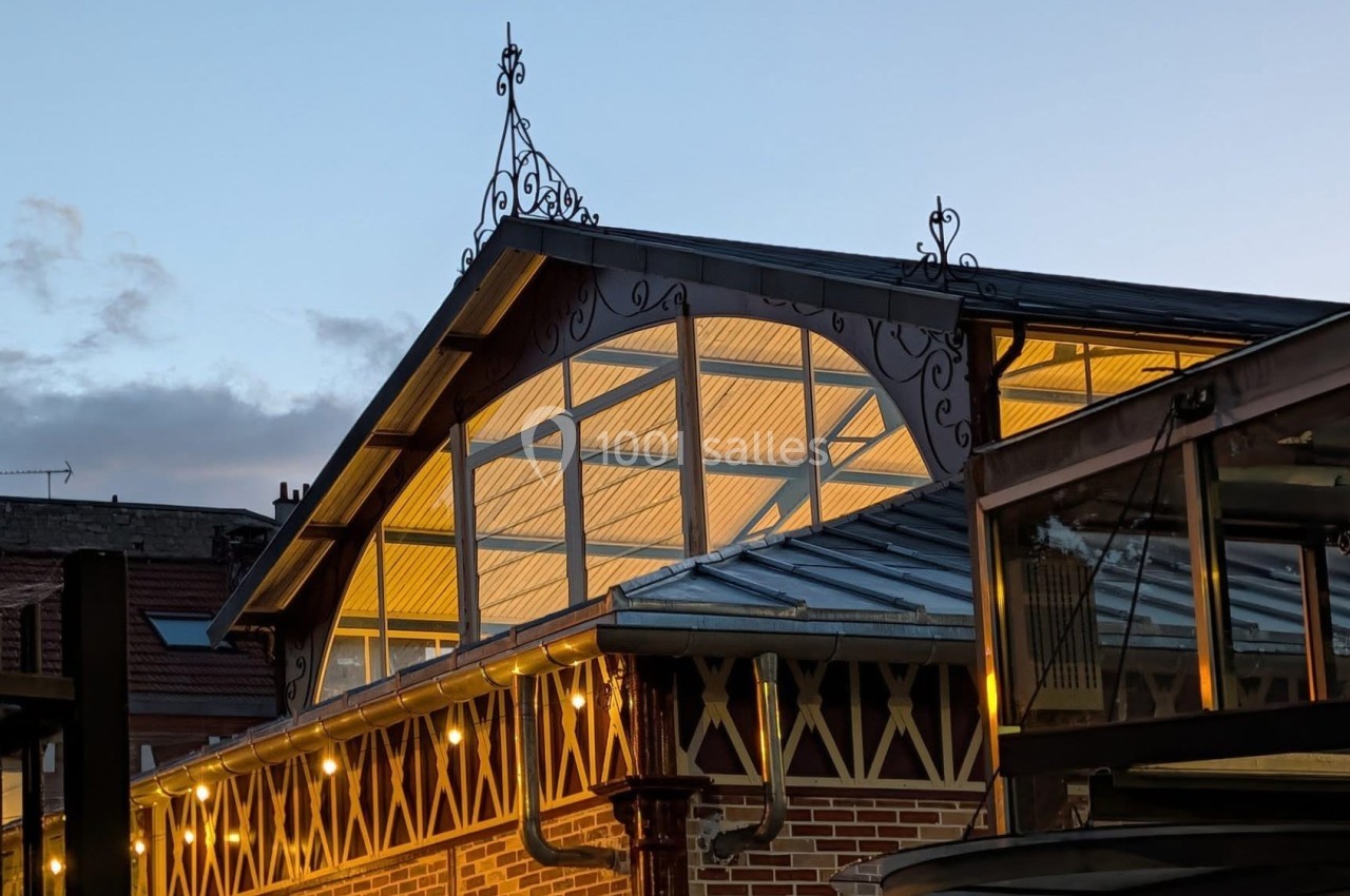 Toit d'un bâtiment en briques avec des structures métalliques et des lumières allumées au crépuscule.