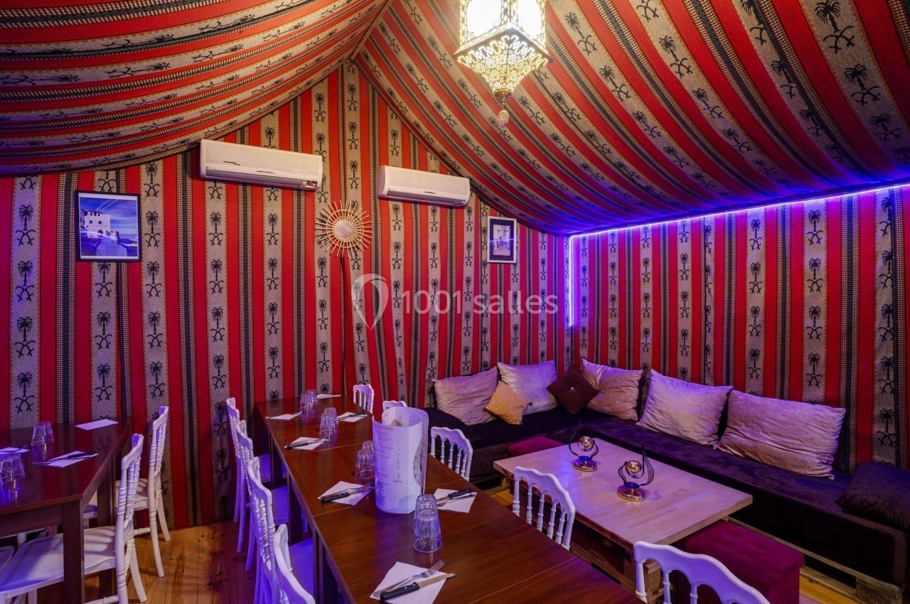Salle décorée dans un style oriental avec des banquettes, des coussins, une table en bois et un éclairage tamisé.