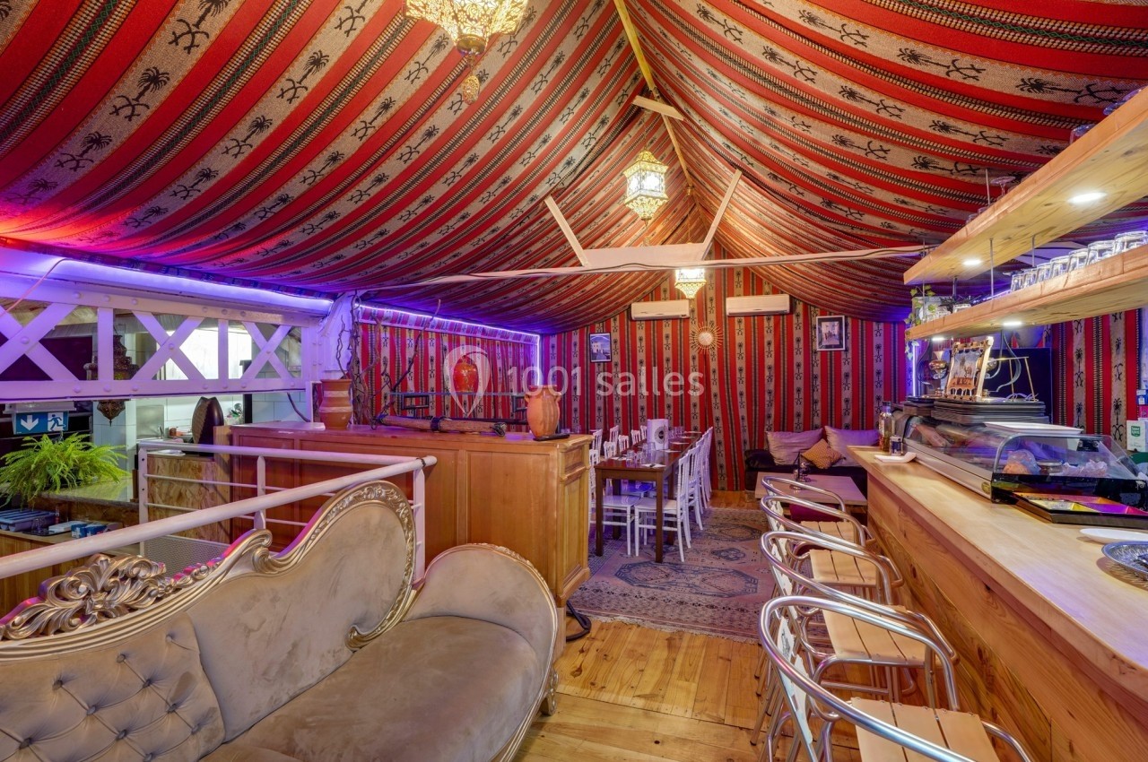 Intérieur d'un restaurant décoré dans un style oriental avec des motifs rouges, un bar en bois et des tables alignées.