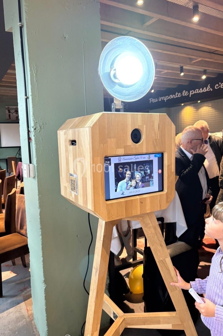 Borne photo en bois avec écran tactile et éclairage, utilisée lors d'un événement dans un espace intérieur.