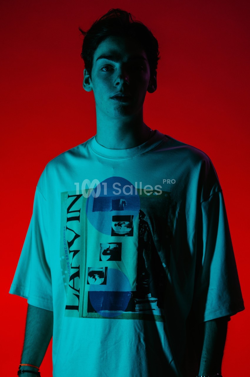 Un homme portant un t-shirt imprimé, éclairé par une lumière rouge et bleue dans un environnement sombre.