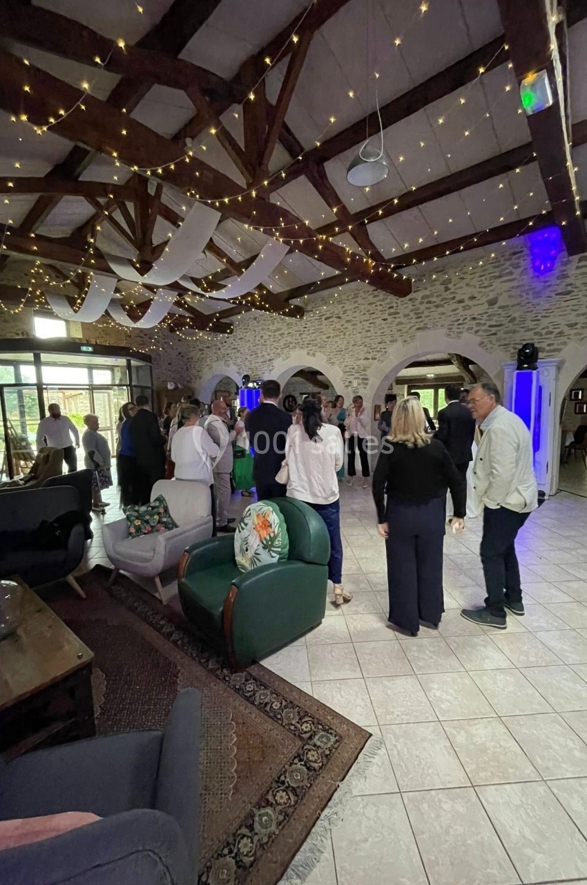 Groupe de personnes debout dans une salle avec poutres apparentes, guirlandes lumineuses et mobilier confortable.
