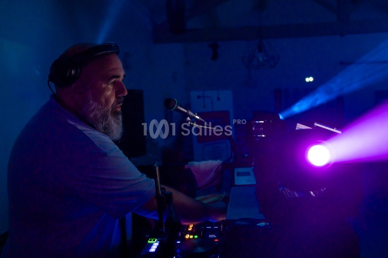 Un DJ mixe de la musique dans une ambiance sombre, éclairé par des projecteurs colorés.