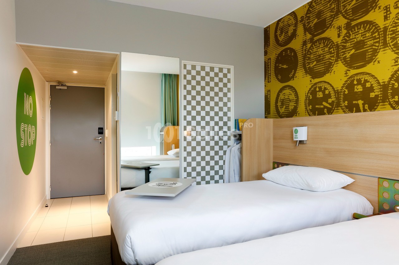 Deux lits simples dans une chambre moderne avec décorations murales colorées et lumière naturelle.
