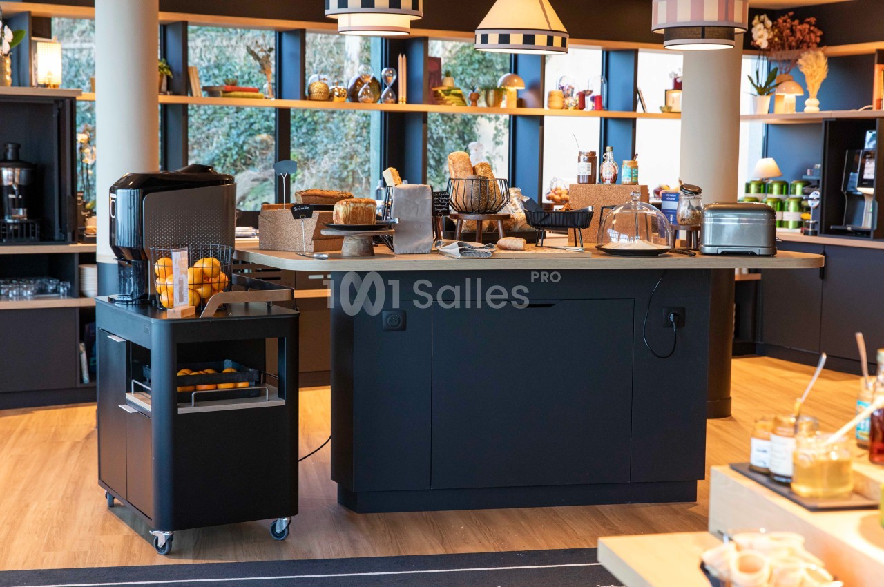 Buffet de petit-déjeuner avec grille-pain, viennoiseries, jus d'orange et équipements de cuisine sur un comptoir moderne.