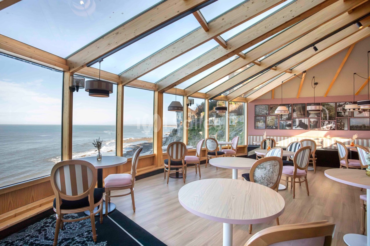 Salle lumineuse avec vue sur la mer, grandes baies vitrées, mobilier en bois clair et ambiance chaleureuse.