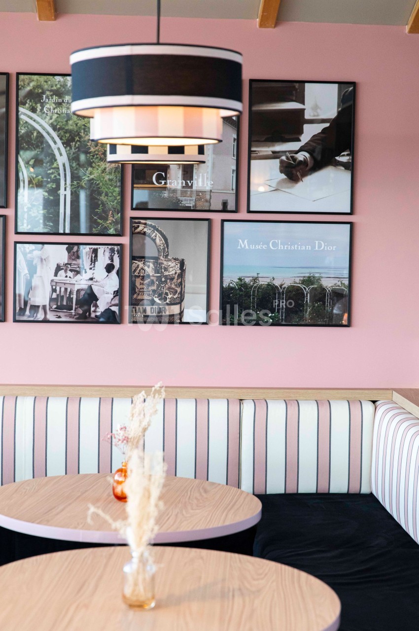 Banquette rayée et tables en bois clair dans un café décoré de cadres photos sur un mur rose.