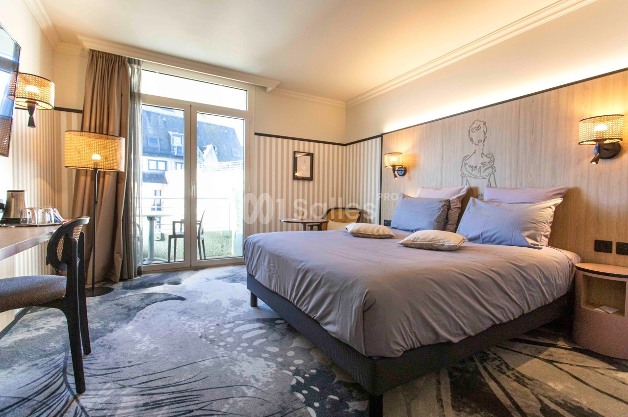 Chambre d'hôtel lumineuse avec un grand lit, décoration moderne, bureau, et balcon donnant sur l'extérieur.