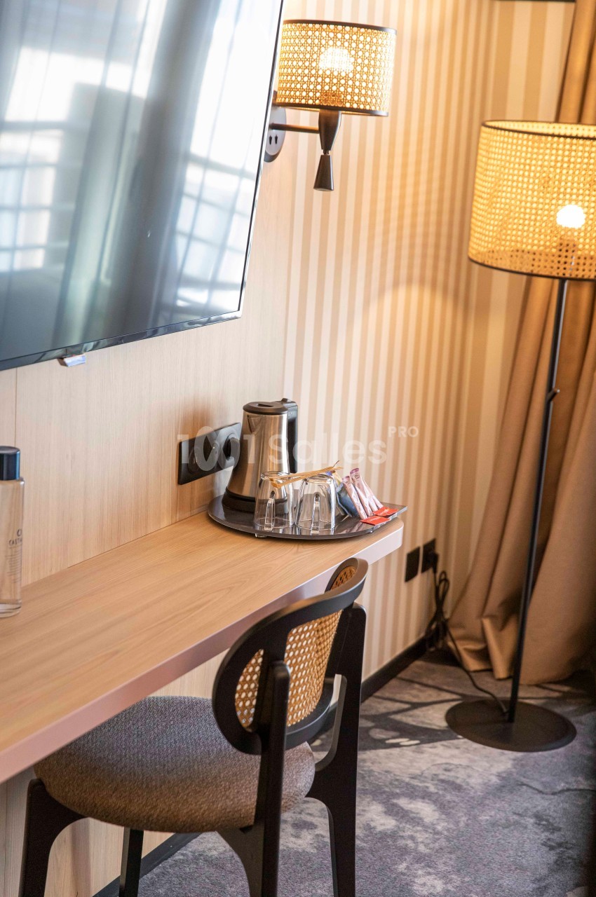 Bureau en bois avec chaise, lampe, télévision murale, bouilloire et verres, dans une pièce à la décoration moderne.