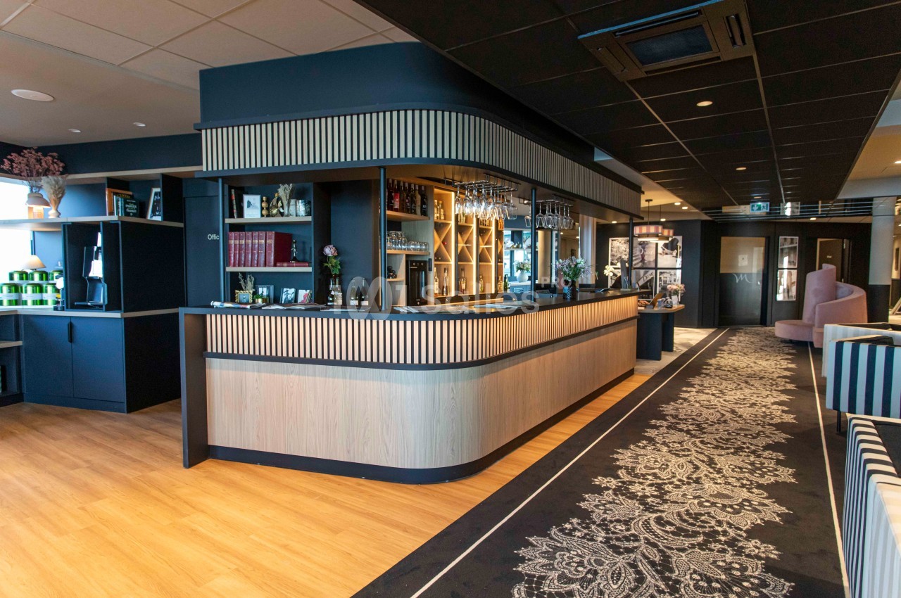 Comptoir de bar moderne en bois clair avec étagères décoratives, dans un espace intérieur élégant et bien éclairé.
