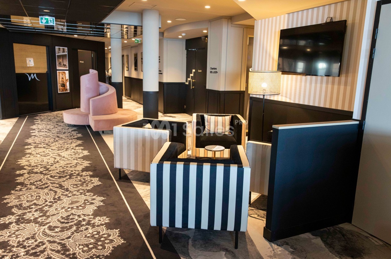 Espace salon avec fauteuils rayés, table basse, lampadaire et télévision, dans un couloir au décor moderne et élégant.