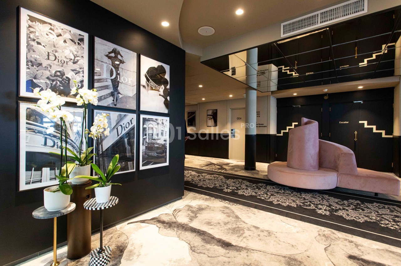 Intérieur d'un espace moderne avec des affiches murales, des orchidées en pot et des sièges rose pâle sur un sol décoratif.