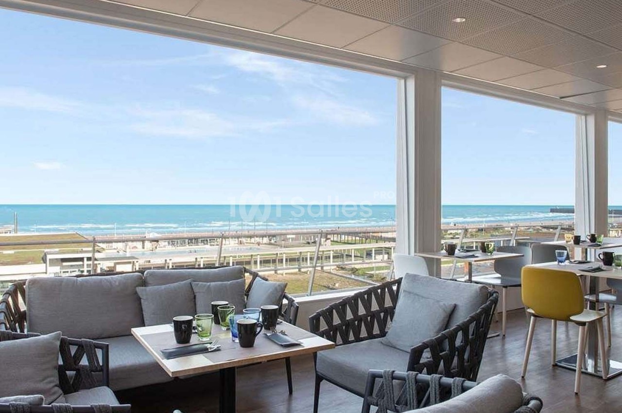 Salle de restaurant lumineuse avec vue panoramique sur la mer, mobilier moderne et tables dressées.