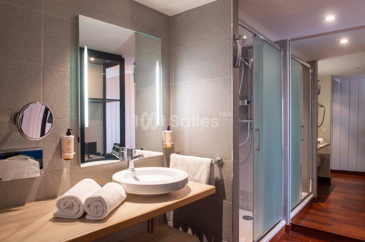 Salle de bain moderne avec lavabo, miroir éclairé, serviettes pliées et douche vitrée en arrière-plan.