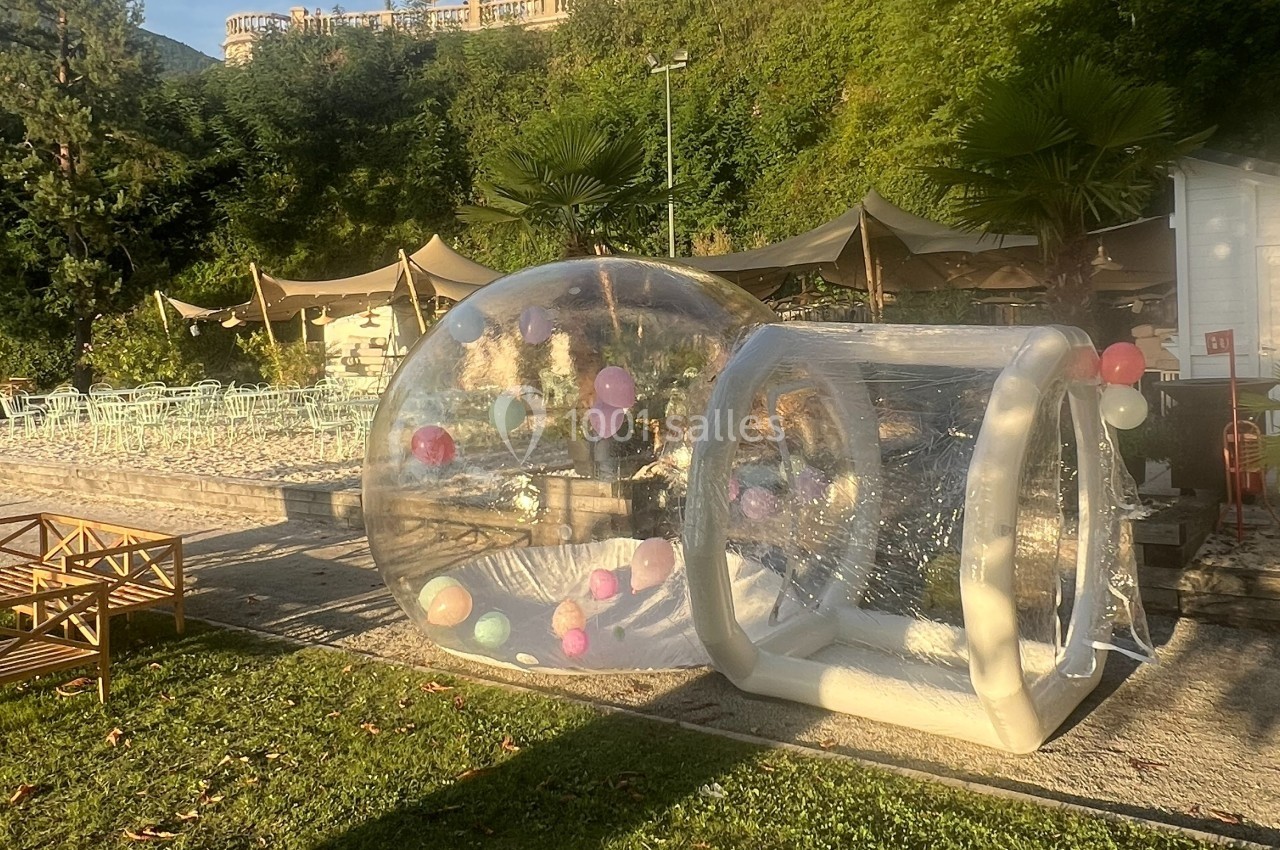 Structure gonflable transparente avec des ballons colorés à l'intérieur, installée dans un espace extérieur verdoyant.
