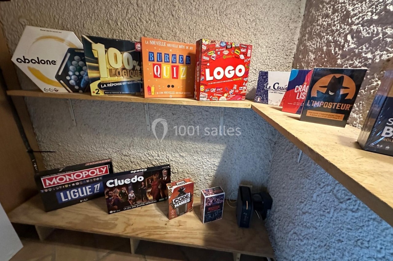 Jeux de société variés disposés sur des étagères en bois contre un mur texturé.