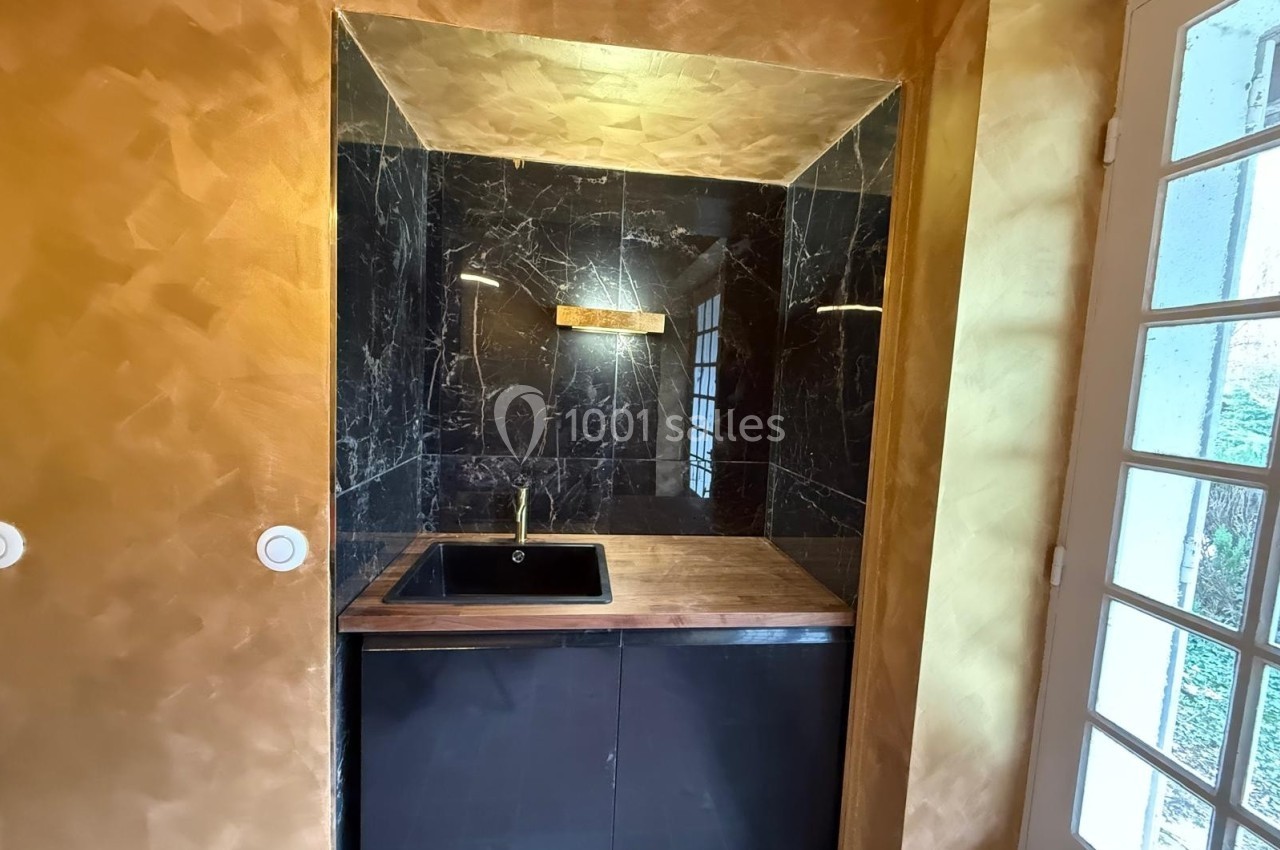 Petit espace lavabo avec évier noir, plan de travail en bois, murs en marbre noir et éclairage intégré.