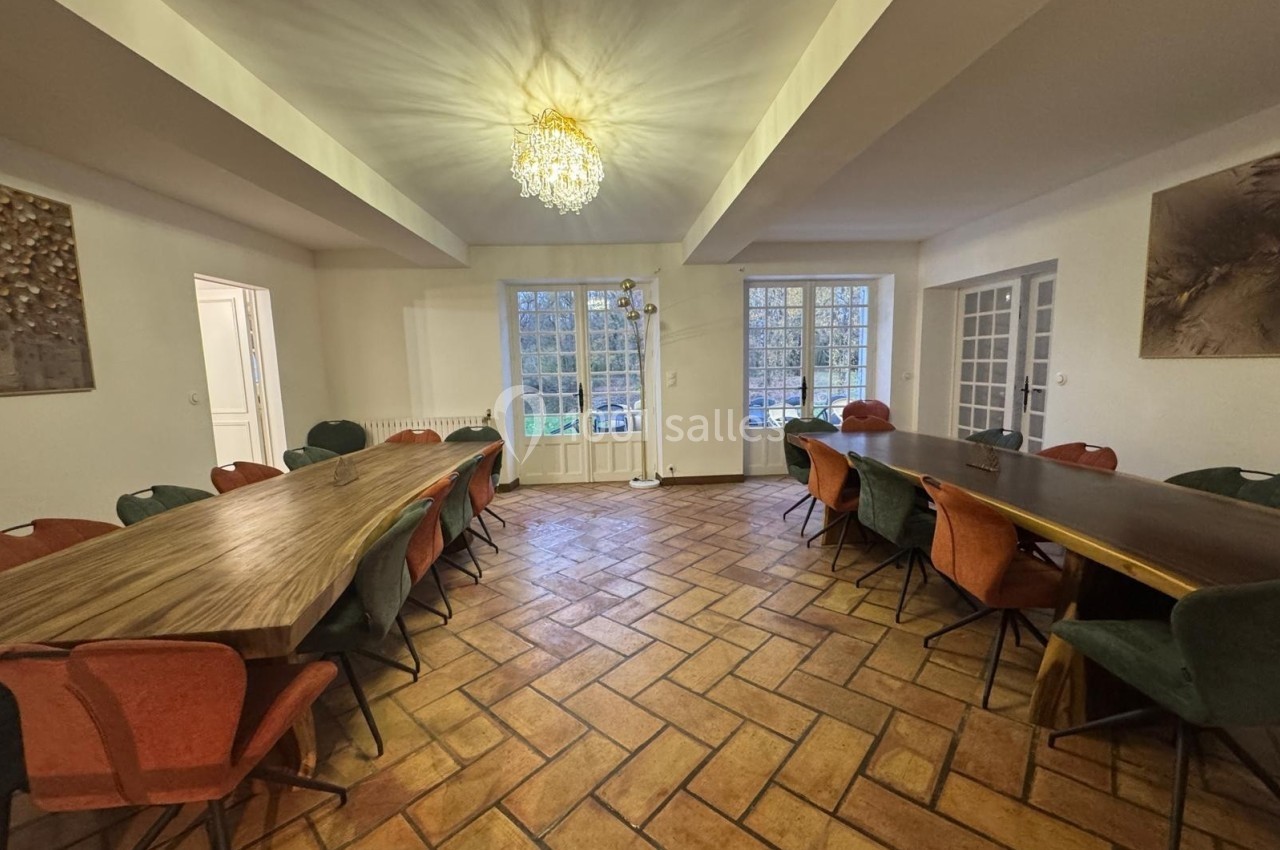 Salle de réunion lumineuse avec deux grandes tables en bois, des chaises colorées et un sol en carrelage.