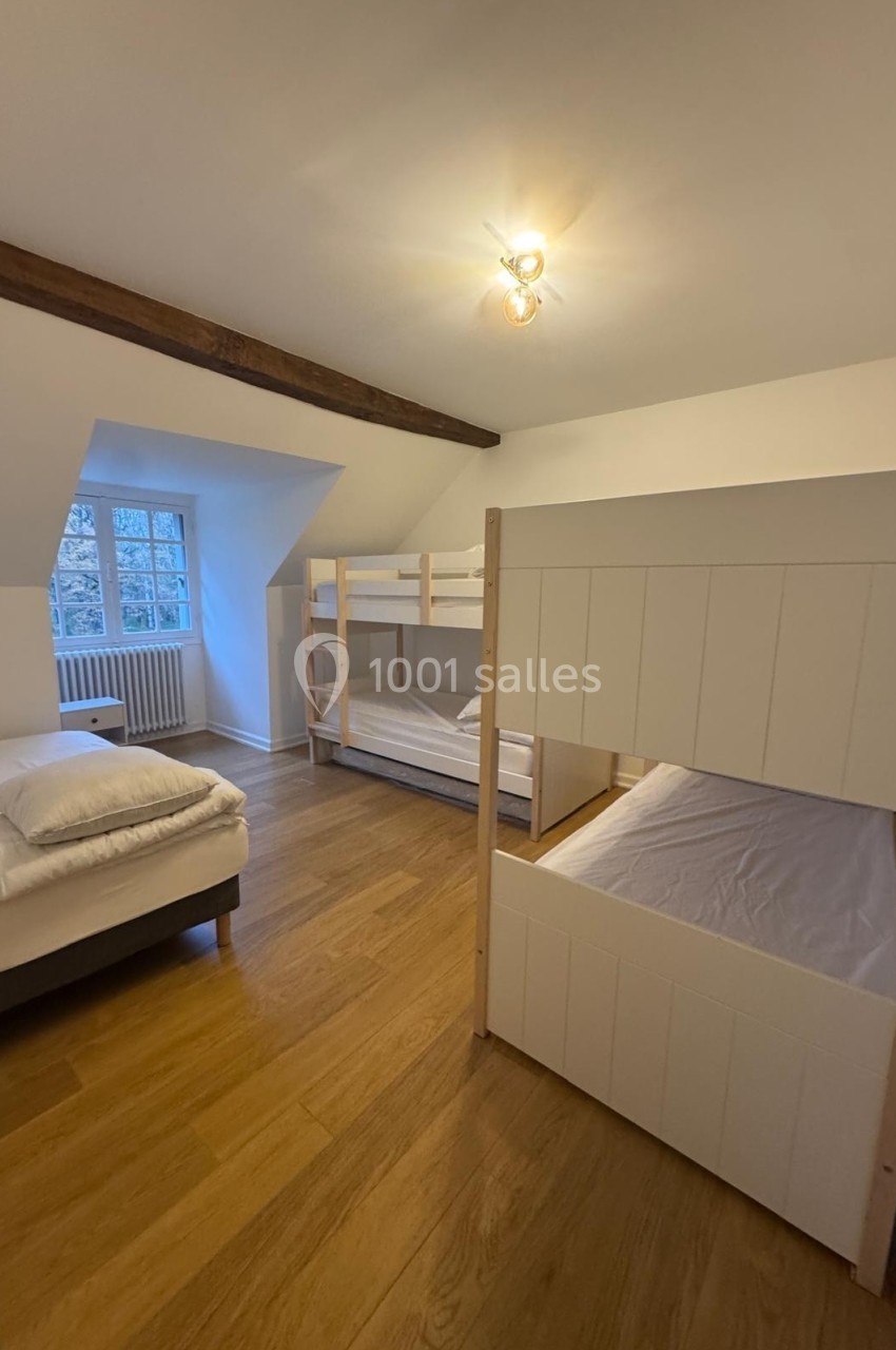 Chambre avec parquet, un lit double et deux lits superposés en bois blanc, éclairée par une fenêtre et une lampe au plafond.