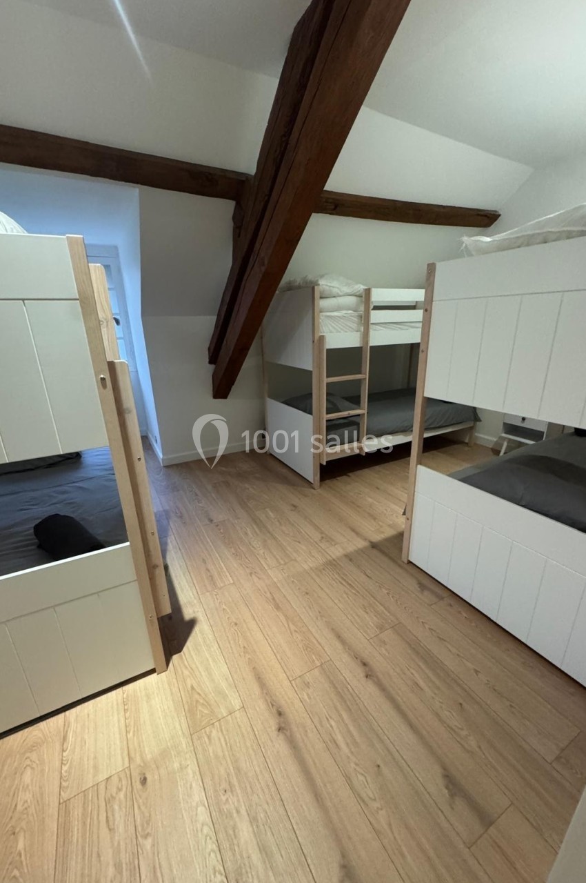 Chambre avec parquet, lits superposés blancs en bois clair et poutres apparentes sous un plafond mansardé.
