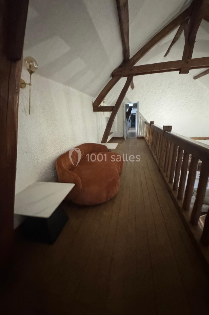 Canapé orange et table basse blanche sur un parquet en bois, dans un couloir mansardé avec poutres apparentes.