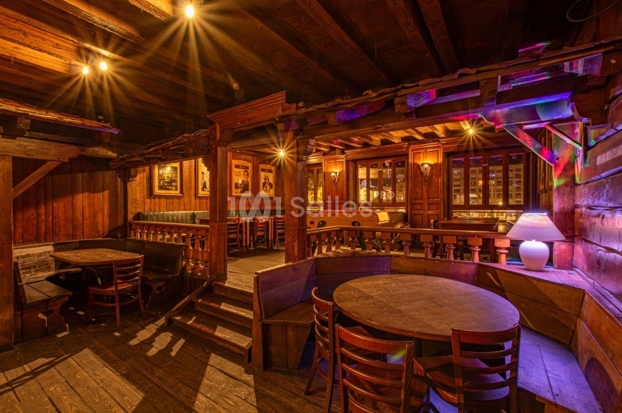 Intérieur d'un restaurant en bois avec tables rondes, chaises, éclairage chaleureux et ambiance rustique.