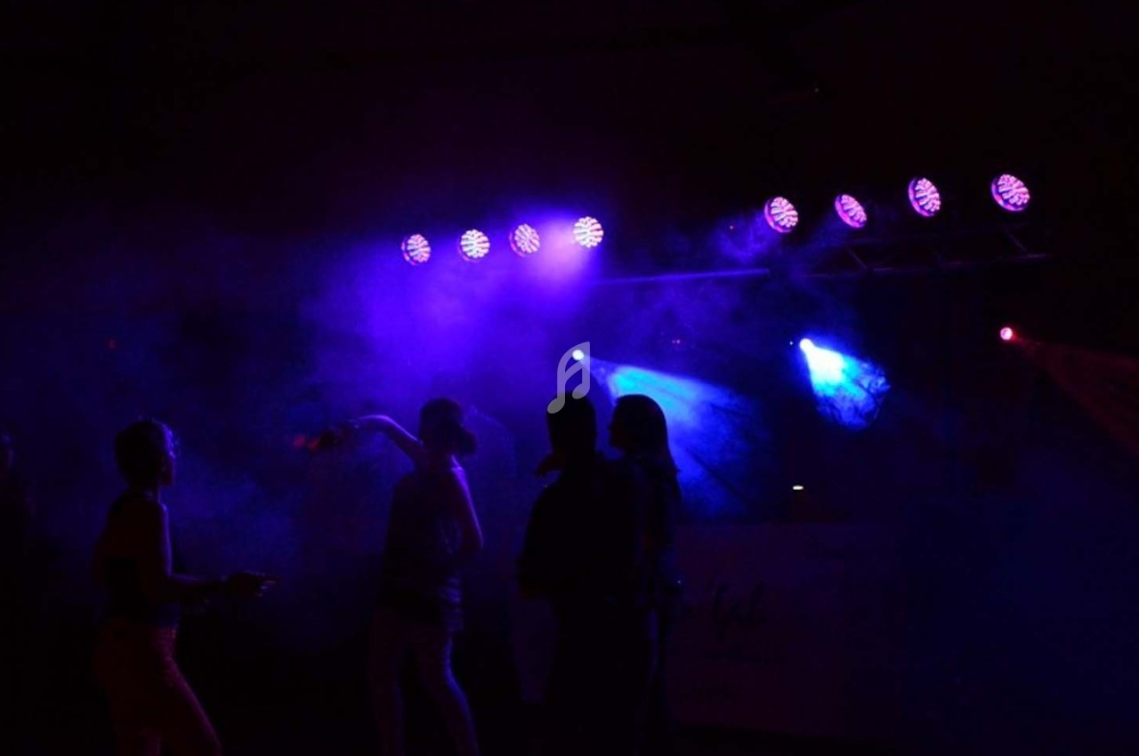 Personnes dansant dans une ambiance sombre avec des lumières violettes et bleues éclairant la scène.