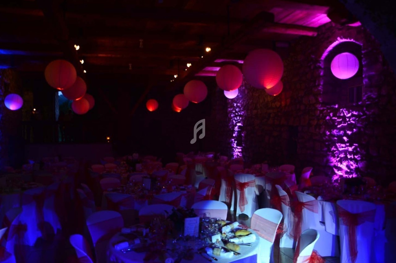 Salle de réception décorée avec des lanternes rouges suspendues, éclairage tamisé violet et tables dressées pour un…
