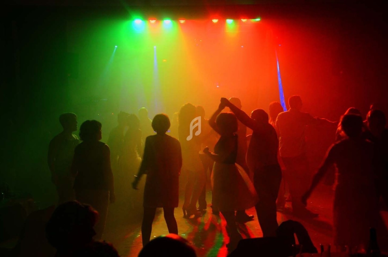 Personnes dansant dans une salle sombre éclairée par des lumières colorées rouge, verte et bleue.