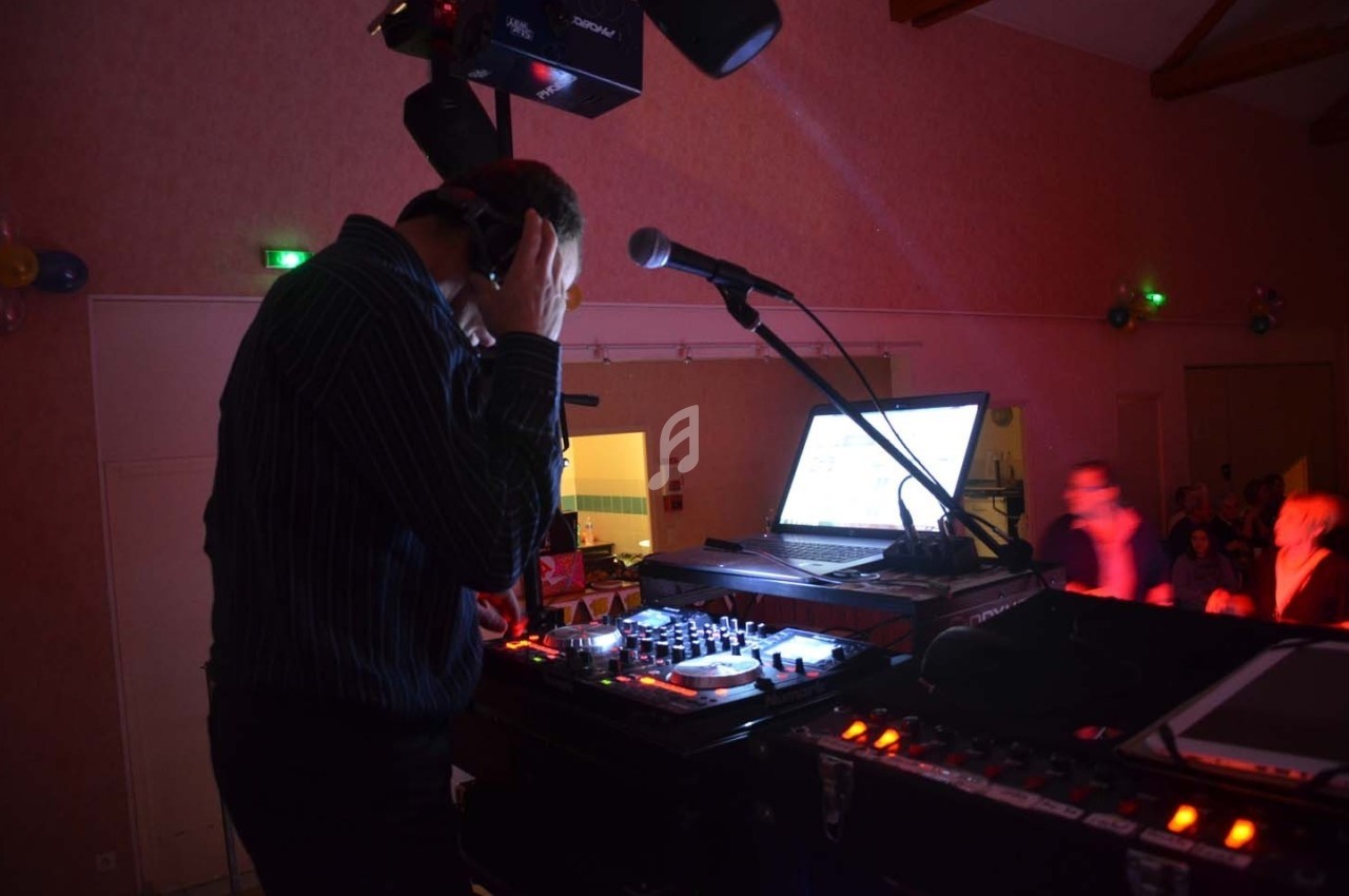Un DJ mixe de la musique sur une console éclairée, avec un ordinateur portable et un micro à proximité.